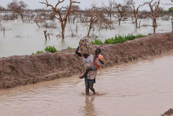 People displaced by flooding carry children and belongings along a waterlogged road in Bentui, South Sudan. (file)
