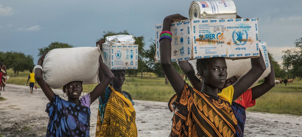 En Sudán del Sur, las mujeres transportan cajas de ayuda alimentaria sobre sus cabezas a lo largo de un camino de tierra.