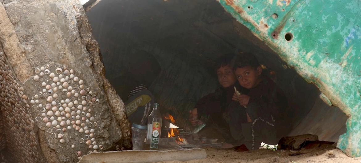 As rain falls over Gaza, children take refuge beneath a disabled fishing boat, one of the few places offering shelter in the overcrowded displacement area.