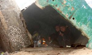 As rain falls over Gaza, children take refuge beneath a disabled fishing boat, one of the few places offering shelter in the overcrowded displacement area.