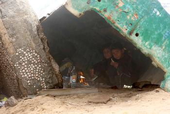 As rain falls over Gaza, children take refuge beneath a disabled fishing boat, one of the few places offering shelter in the overcrowded displacement area.