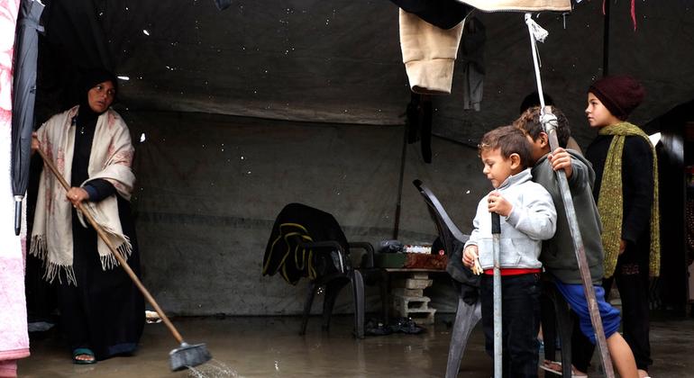 نازحة تقوم بدفع مياه الأمطار خارج خيمتها التي غمرتها سيول الليلة الماضية، بينما يقف أطفالها إلى جانبها في أحد مواقع النزوح في غزة، في وقت تفاقمت فيه الظروف المعيشية القاسية أصلا.