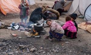 As crianças usam o calor de um fogão a lenha para se manterem aquecidas no duro inverno afegão.