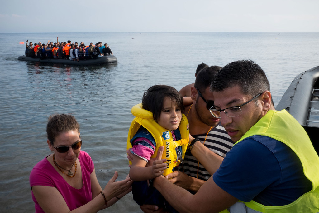 Une volontaire de UNICEF aide une jeune réfugiée, portant un gilet de sauvetage, à débarquer d'un canot pneumatique près de Mithymna, sur l'île de Lesbos, en Grèce. Un autre bateau transportant des réfugiés est visible à l'arrière-plan.