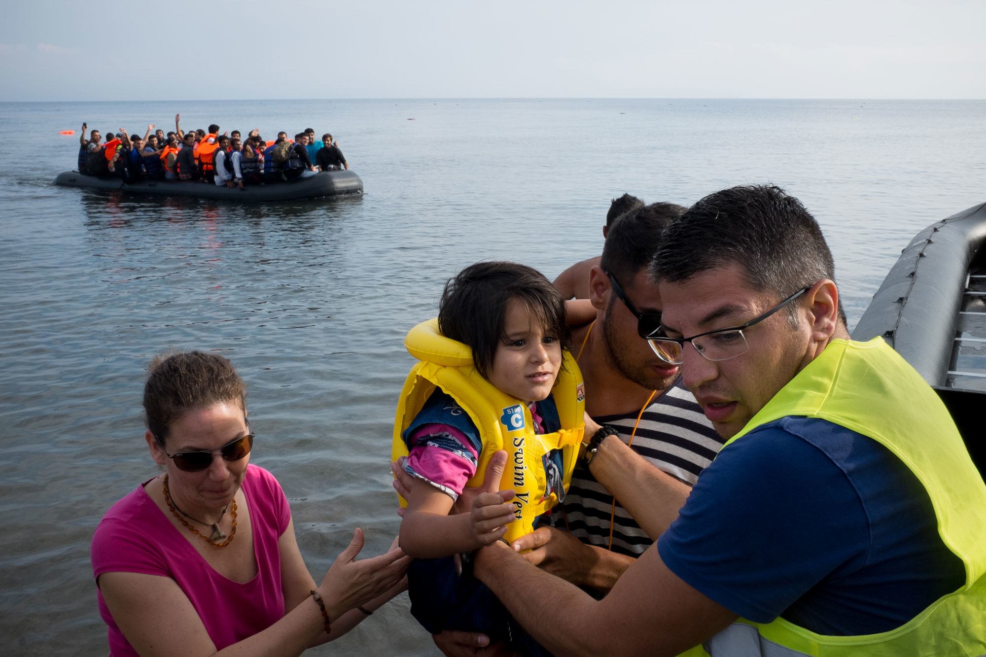 من الأرشيف: متطوع يساعد اللاجئين الوافدين حديثاً على النزول من قارب مطاطي كبير في جزيرة ليسبوس في منطقة شمال بحر إيجه. 