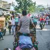 A man pedals a traditional Becak rickshaw down a busy street in Bandung City, Indonesia.