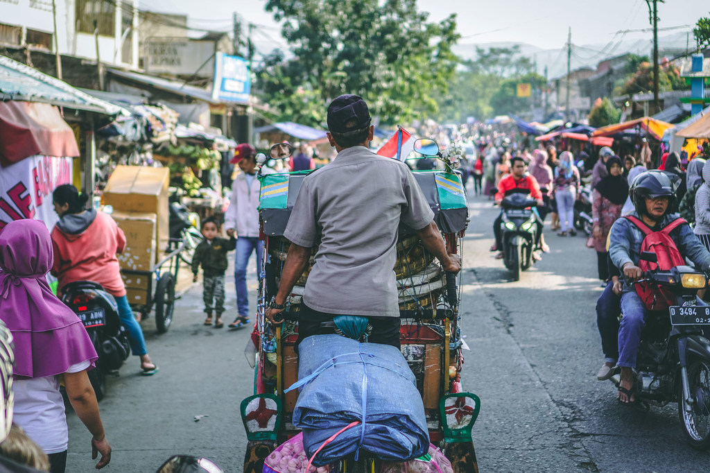 在印度尼西亚万隆市，一名男子在繁忙的街道上蹬着一辆传统的贝卡人力车。