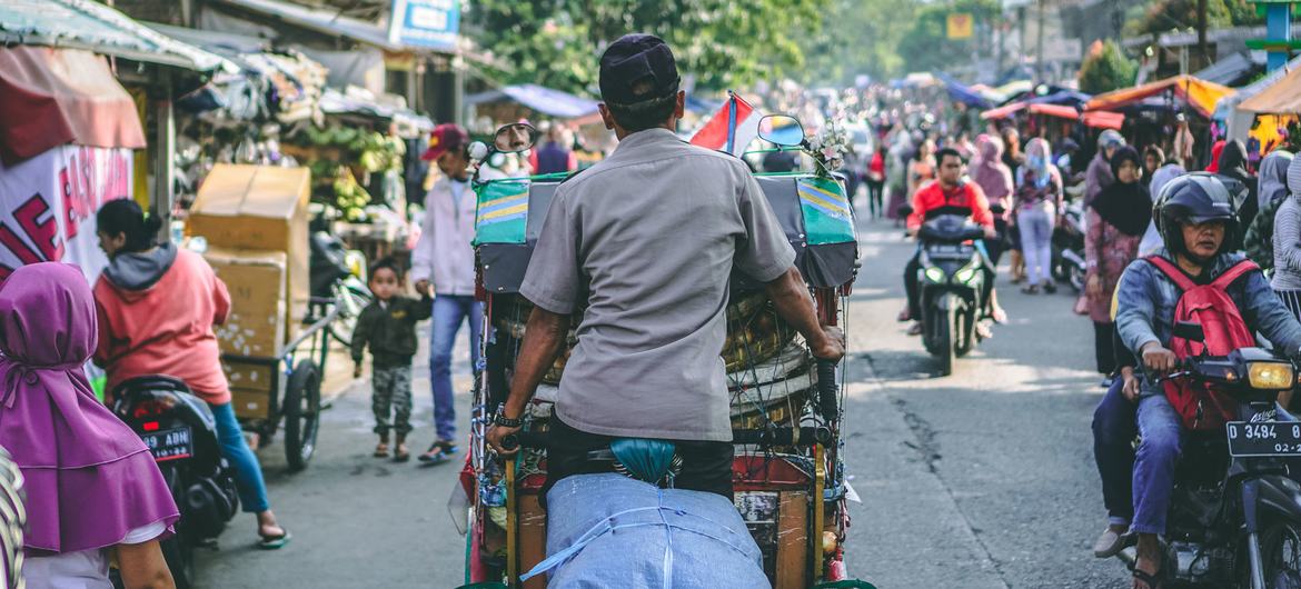 在印度尼西亚万隆市，一名男子在繁忙的街道上蹬着一辆传统的贝卡人力车。