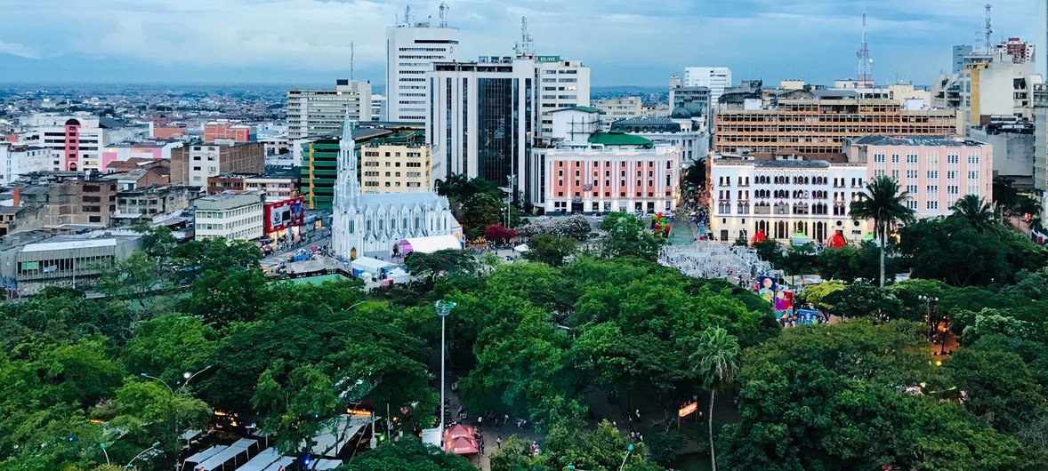 Vista aérea de un parque y una plaza en Cali, Colombia, rodeados de edificios al atardecer.