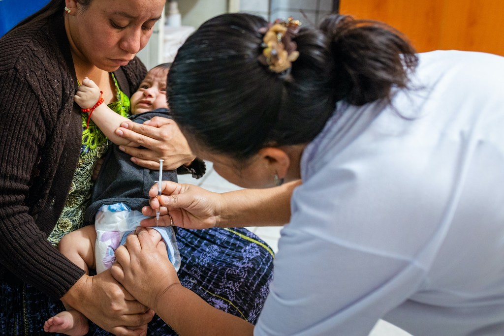 Un trabajador de la salud administra una vacuna a un bebé que llora, sostenido por su madre, en un centro de atención primaria en San Pedro Carchá, Guatemala.