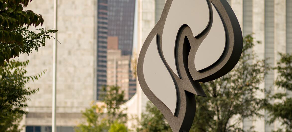 يظهر تمثال كويبوكا التذكاري لشعلة الأمل في المقدمة مع مقر United Nations وعلم الأمم المتحدة في الخلفية في نيويورك.