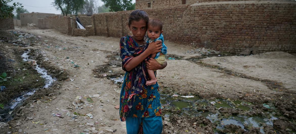 在村庄被洪水摧毁后，巴基斯坦一名年轻女孩抱着一个孩子前往一家流动医疗诊所。