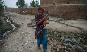 A young girl holds a child as she makes her way to a mobile health clinic after their village was devasted by the floods in Pakistan.