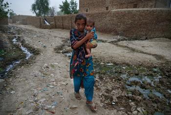 فتاة صغيرة تحمل طفلًا وهي تشق طريقها إلى عيادة صحية متنقلة بعد أن دمرت الفيضانات قريتهم في باكستان.