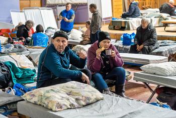 Refugiados aguardam em um centro de trânsito em Pavlohrad, Ucrânia, em 13 de janeiro de 2025. Um homem e uma mulher idosos sentam-se em um colchão, cercados por outros deslocados internos e seus pertences.