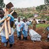 Washiriki wa timu ya Msalaba Mwekundu wakiwa wamevaa mavazi ya kujikinga na fulana wakiwa wamebeba majembe na jeneza katika eneo la mazishi katika makaburi ya Kitatumba, Butembo, DRC, kama sehemu ya kukabiliana na Ebola.