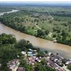 Vista aérea de un río sinuoso en la región del Catatumbo, en Colombia, con un pequeño pueblo y campos verdes en primer plano.