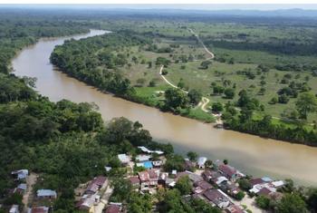 Vista aérea de un río sinuoso en la región del Catatumbo, en Colombia, con un pequeño pueblo y campos verdes en primer plano.