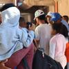 Un hombre lleva a un niño en una sudadera gris mientras espera en fila con otras personas desplazadas en un campamento de refugiados en Cúcuta, Colombia. La escena refleja los esfuerzos de ayuda humanitaria de ACNUR durante la crisis migratoria.