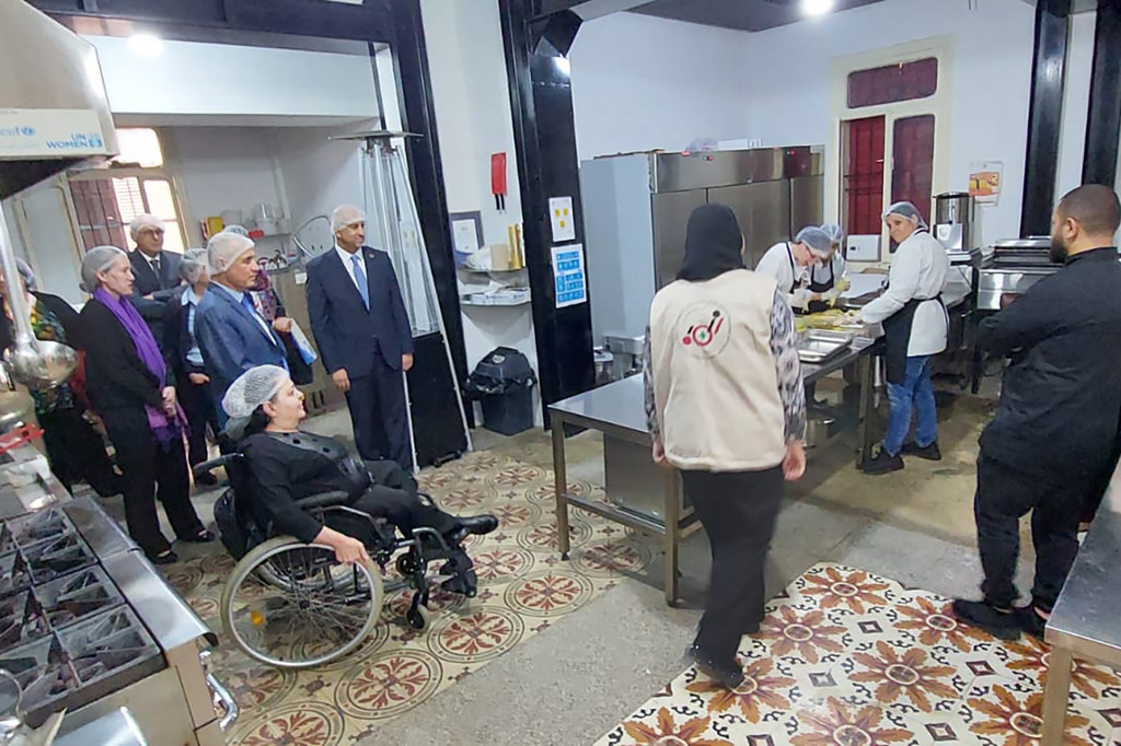 UN Secretary-General Amina Mohammad and other officials visit the Access Kitchen project in Lebanon, engaging with women with disabilities. The scene shows a commercial kitchen where staff are preparing food.