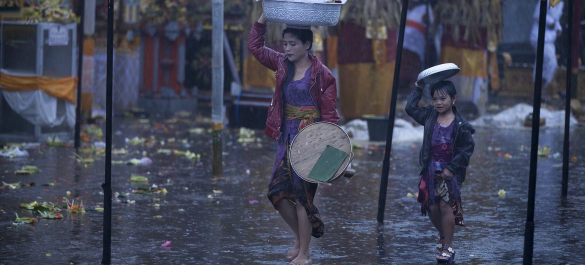 A mother and her daughter try to shield themselves from rain as they walk in a market.