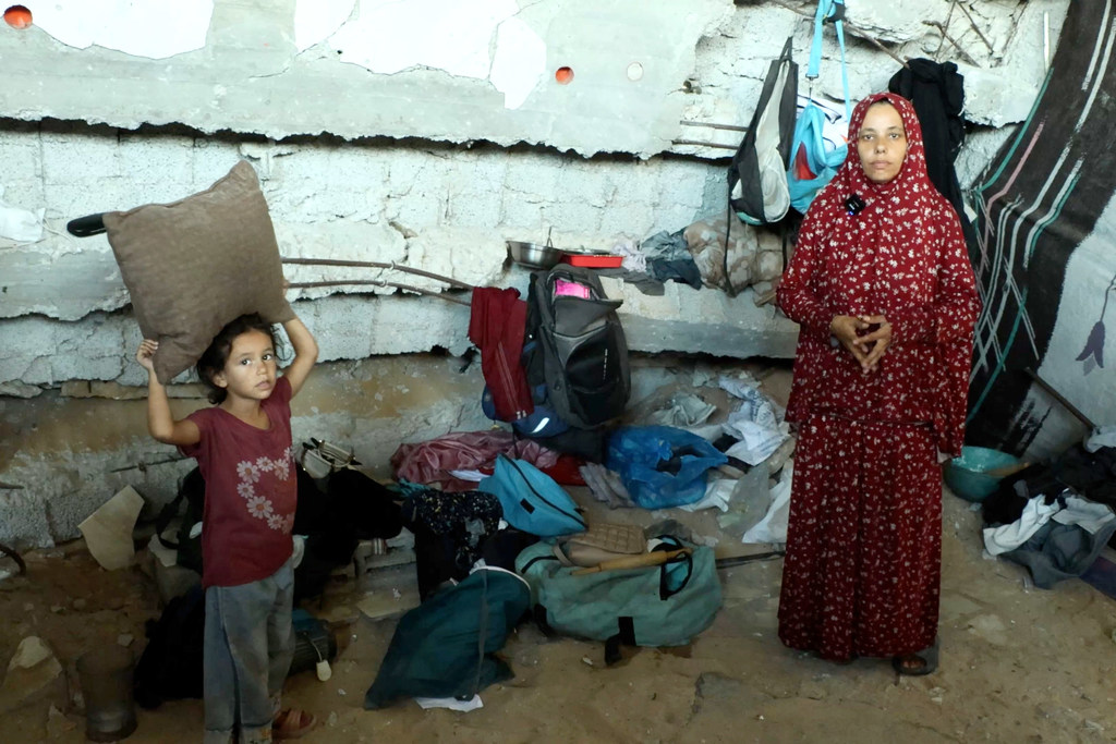 Mãe e filha em frente a um prédio destruído