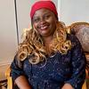 Esther Karin Mngodo, mjumbe wa kamati ya Tuzo ya Kitaifa ya Mwalimu Nyerere ya Uandishi wa Ubunifu nchini Tanzania, ameketi na kutabasamu mbele ya kamera.