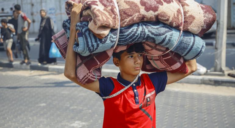 A 14-year-old boy carries mattresses and blankets on his head while his family follows him to an emergency shelter in the Gaza Strip.