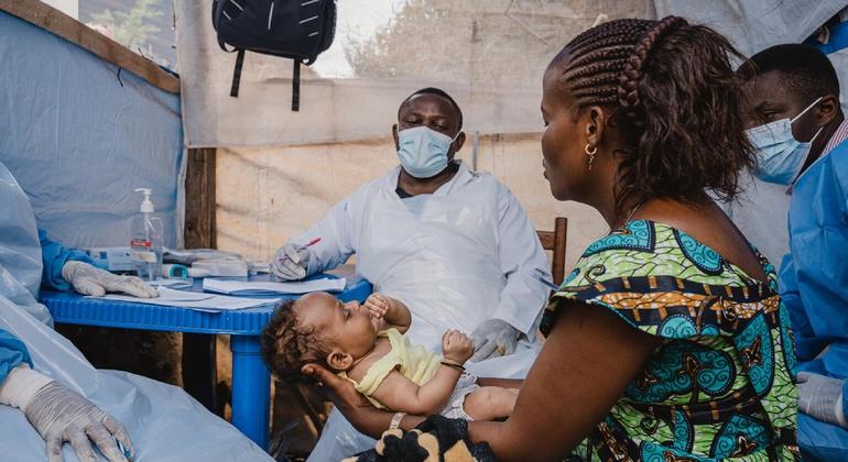 Mama akiwa amembeba mtoto wake huku mfanyakazi wa afya akimsajili katika kituo cha mahema nchini DR Congo.