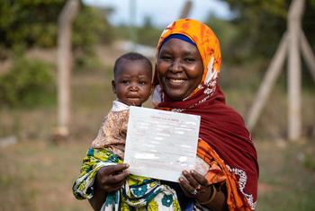 سيدة من مجتمع بيمبا في كينيا سعيدة بالحصول على شهادة ميلاد لابنتها.