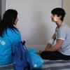 Сотрудник UNICEF сидит на больничной койке и разговаривает с раненым украинским мальчиком, у которого на лице и руке повязки.