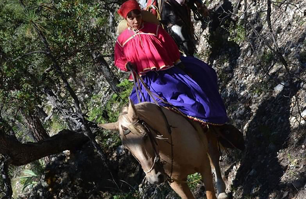 Una enfermera vestida con ropa tradicional cabalga a caballo por una zona montañosa.