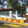 La entrada de una escuela en Paraguay cuenta con un paso de peatones marcado con pintura amarilla para carreteras y una hilera de neumáticos pintados de colores que sirven como macetas. Se puede ver un letrero de madera con el logotipo "mi camino escolar seguro".