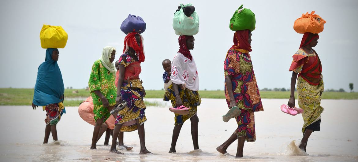 Women walk across a body of water in Rann, Borno State, Nigeria.