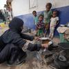 A mother-of-nine, who is suffering from malnutrition, cooks a meal for her children in a displaced camp in Aden, Yemen.
