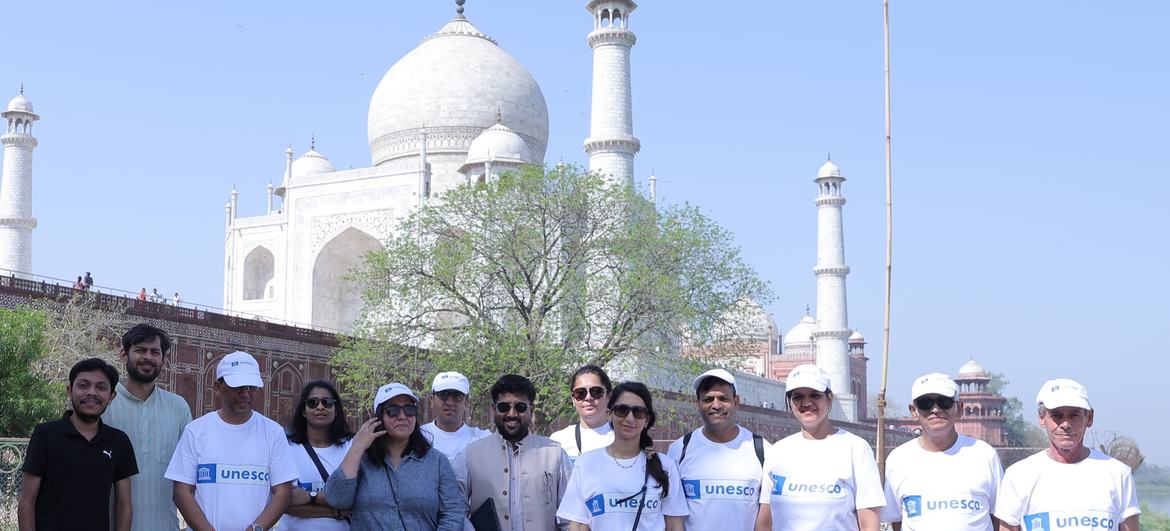 कुछ लोग, जिनमें से कुछ ने UNESCO के लोगो वाली सफेद टी-शर्ट पहनी हुई है, ताजमहल के सामने भारतीय ध्वज के लहराते हुए फोटो खिंचवा रहे हैं।