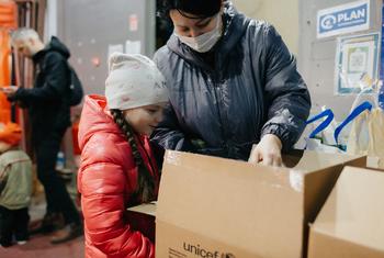 यूक्रेन के चेरनिहीव में एक माँ-बेटी, नए कपड़ों के एक डिब्बे को खोल रही हैं, जिसे मोल्दोवा में यूनीसेफ़ और साझेदार संगठनों ने प्रदान किया है.