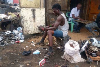 Un jeune homme travaille au milieu de piles de déchets électroniques dans un site de recyclage informel, entouré d'appareils électroménagers jetés et de matières dangereuses.