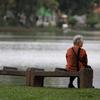 一位泰国老妇人独自坐在池塘边的长椅上。