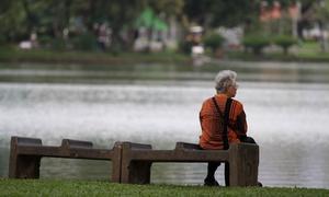 Una mujer mayor está sentada sola en un banco cerca de un estanque.