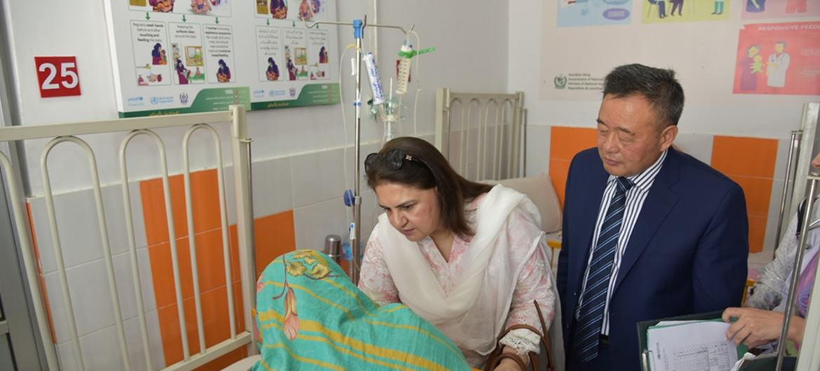 سوٹ میں ملبوس ایک عورت اور ایک مرد ہسپتال کے بستر پر ایک شیر خوار بچے سے ملاقات کر رہے ہیں۔