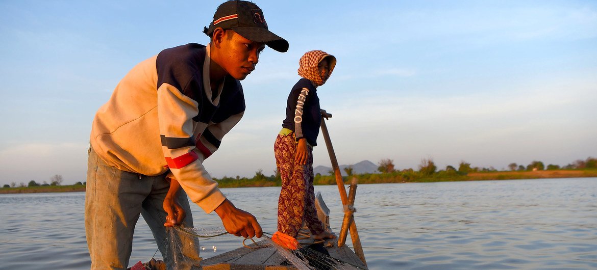 Homem e menino em um barco em um rio no Camboja, puxando uma rede de pesca.