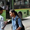 Две девушки стоят на улице в Дели, Индия, перед зеленым автобусом и смотрят в мобильный телефон.