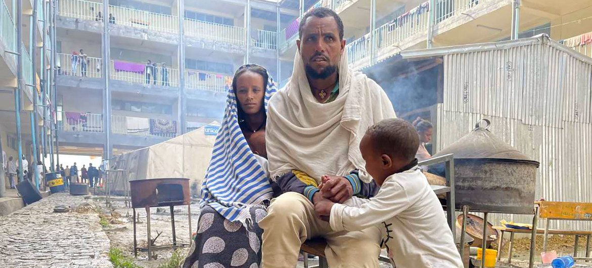 A displaced family from the Tigray conflict sits outside a temporary shelter in Ethiopia. A man, woman, and young child are pictured.