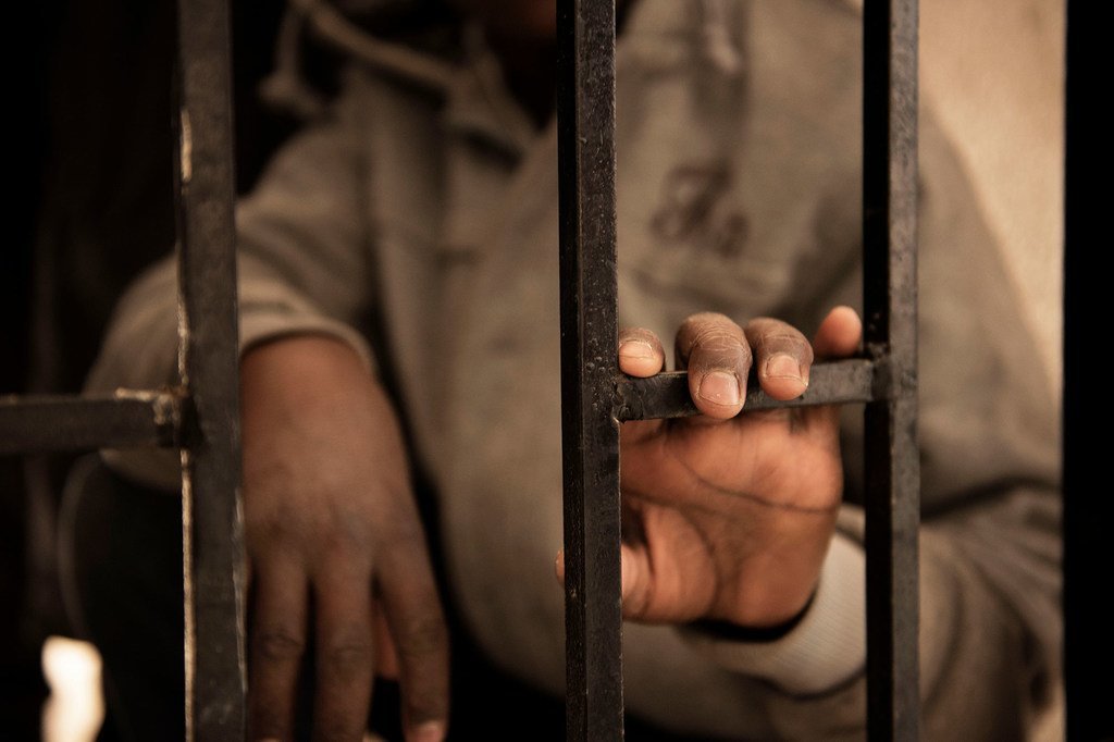 A fourteen-year-old migrant from Niger rests his hand on a gate inside a detention centre, in Libya.