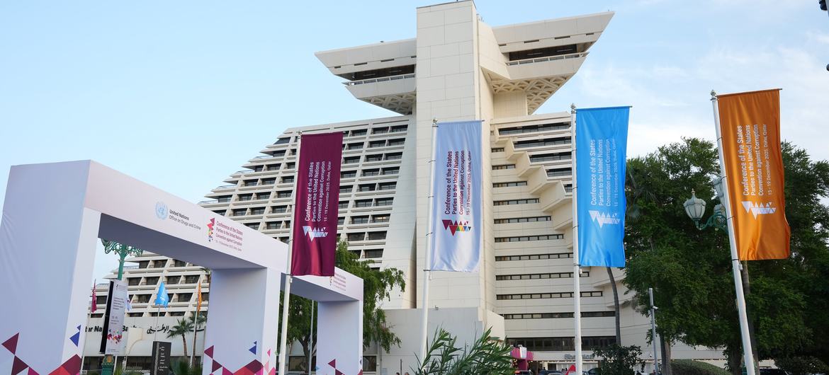 مسرح الجلسة الحادية عشرة لمؤتمر الدول الأطراف في اتفاقية الأمم المتحدة لمكافحة الفساد في الدوحة، قطر، مع لافتات ومبنى حديث.