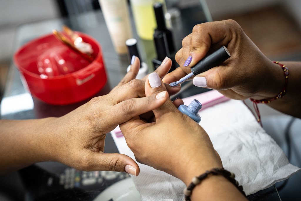 Una persona de piel oscura se está haciendo pintar las uñas con una técnica especializada.