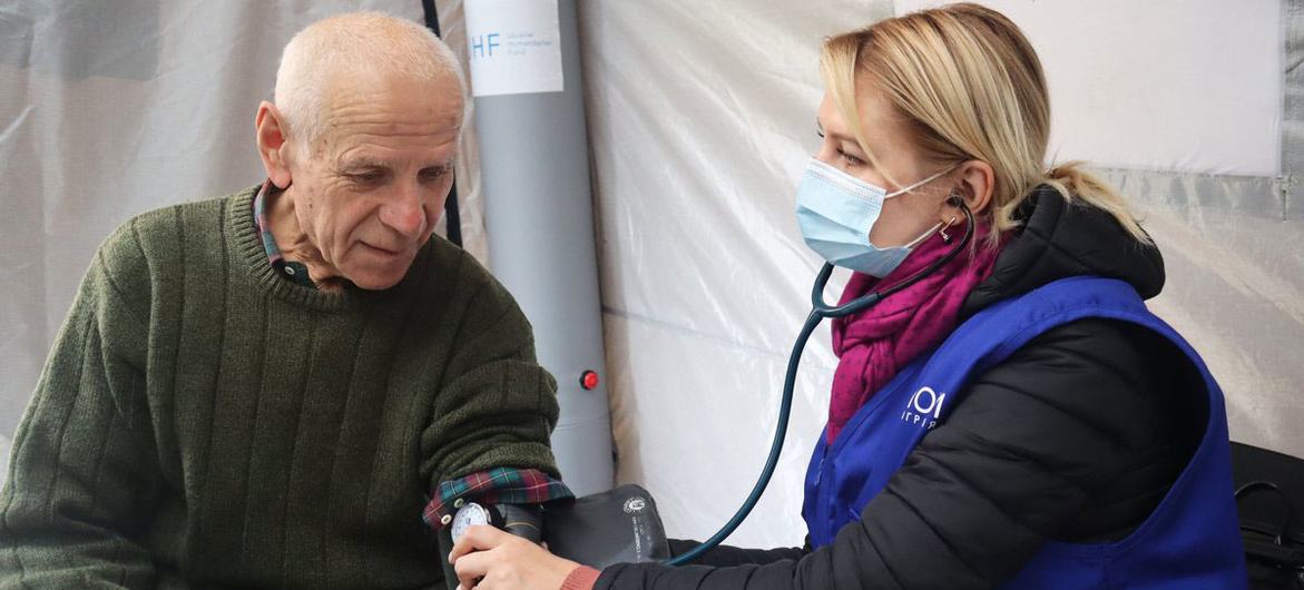 यूक्रेन में एक बुज़ुर्ग व्यक्ति, अन्तरराष्ट्रीय प्रवासन संगठन (IOM) के एक चिकित्सा शिविर में उपचार कराते हुए.