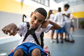 Un niño sonriente en silla de ruedas en el gimnasio de una escuela, participando en una actividad deportiva inclusiva.