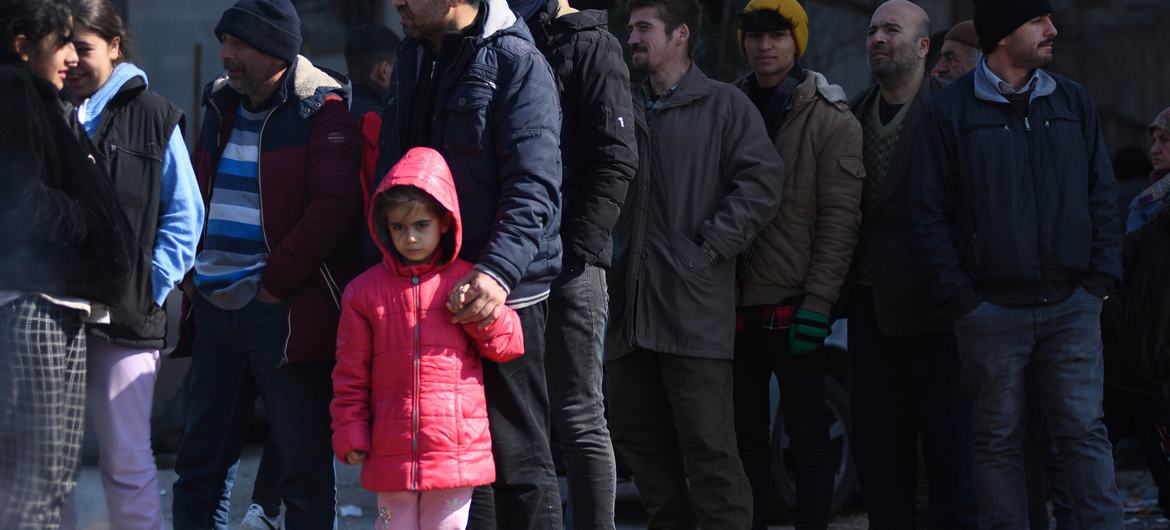 A girl and her father wait in line to receive aid items at a shelter in southeastern Türkiye.